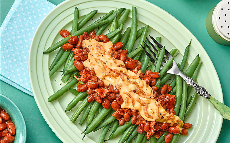 Smoky Smothered Green Beans are plated on a white oval plate alongside a green and silver fork.